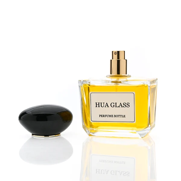 HUA0359 perfume bottle, low rectangular clear glass body with gold neck and a paper label attached, smooth oval pebble plastic cap in navy blue, white, or burgundy, contemporary artistic luxury fragrance packaging design available in 50ml and 100ml