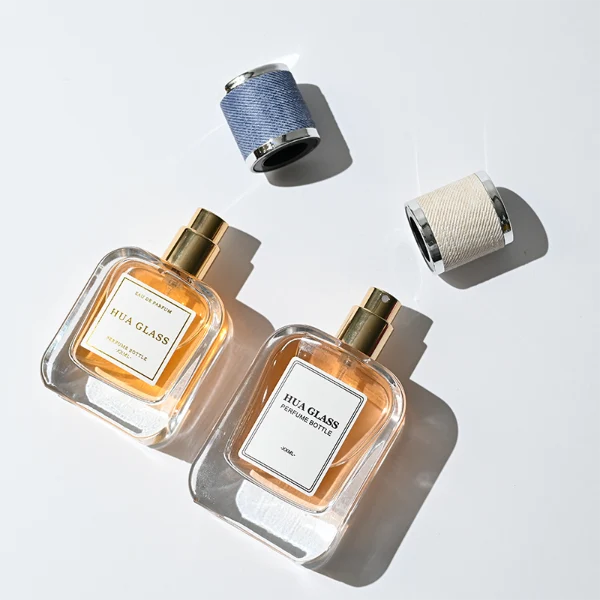 HUA0360 perfume bottle, flat rectangular clear glass body with silver neck and a paper label attached, textured blue or beige cylindrical plastic cap with silver trim, contemporary casual luxury fragrance packaging design available in 30ml, 50ml, and 100ml