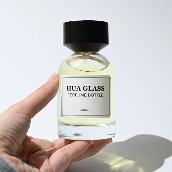 HUA0364 perfume bottle, round cylindrical glass body in translucent grey, red, and blue with gold printed logo, matte black inverted cone plastic cap, contemporary minimalist luxury fragrance packaging design available in 50ml and 100ml
