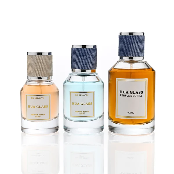 HUA0365 perfume bottle, cylindrical clear glass body with faceted sloped shoulders, silver neck and a paper label attached, textured blue or beige cylindrical plastic cap with silver trim, contemporary casual luxury fragrance packaging design available in 30ml, 50ml, and 100ml