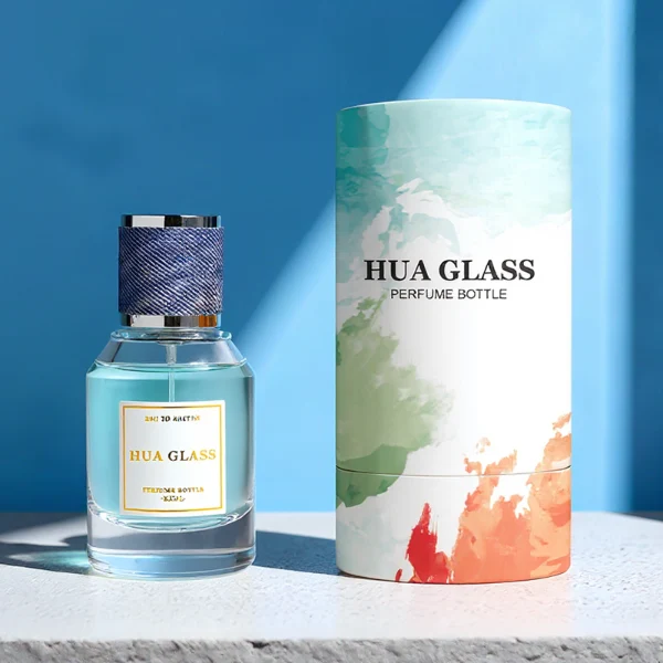 HUA0365 perfume bottle, cylindrical clear glass body with faceted sloped shoulders, silver neck and a paper label attached, textured blue or beige cylindrical plastic cap with silver trim, contemporary casual luxury fragrance packaging design available in 30ml, 50ml, and 100ml