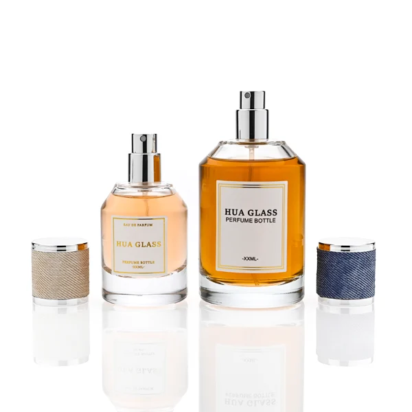HUA0365 perfume bottle, cylindrical clear glass body with faceted sloped shoulders, silver neck and a paper label attached, textured blue or beige cylindrical plastic cap with silver trim, contemporary casual luxury fragrance packaging design available in 30ml, 50ml, and 100ml