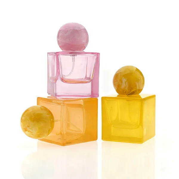 HUA0367 perfume bottle, square cubic glass body in translucent pink or amber orange with gold printed logo, oversized spherical ball plastic cap with marble veins texture, contemporary artistic pop luxury fragrance packaging design available in 30ml, 50ml, and 100ml