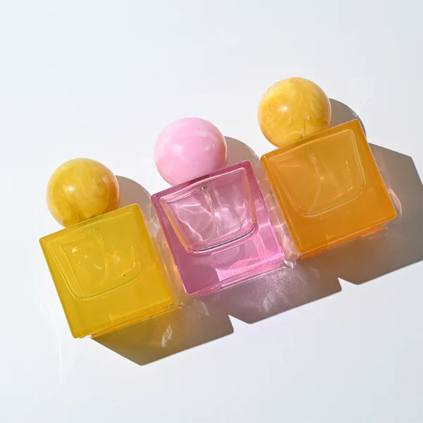 HUA0367 perfume bottle, square cubic glass body in translucent pink or amber orange with gold printed logo, oversized spherical ball plastic cap with marble veins texture, contemporary artistic pop luxury fragrance packaging design available in 30ml, 50ml, and 100ml