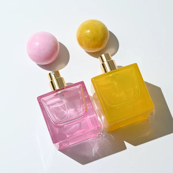 HUA0367 perfume bottle, square cubic glass body in translucent pink or amber orange with gold printed logo, oversized spherical ball plastic cap with marble veins texture, contemporary artistic pop luxury fragrance packaging design available in 30ml, 50ml, and 100ml