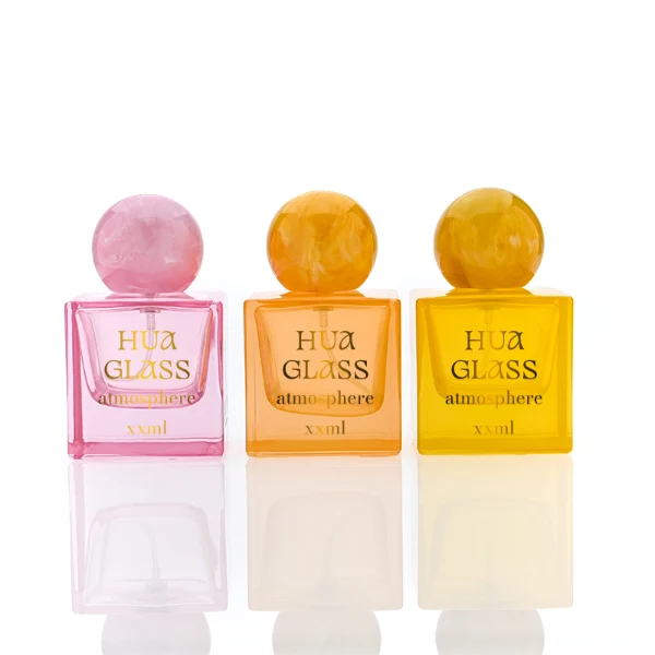 HUA0367 perfume bottle, square cubic glass body in translucent pink or amber orange with gold printed logo, oversized spherical ball plastic cap with marble veins texture, contemporary artistic pop luxury fragrance packaging design available in 30ml, 50ml, and 100ml