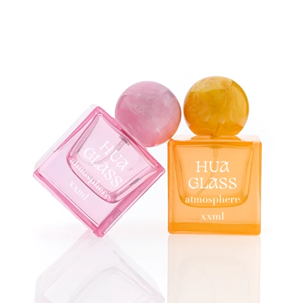 HUA0367 perfume bottle, square cubic glass body in translucent pink or amber orange with gold printed logo, oversized spherical ball plastic cap with marble veins texture, contemporary artistic pop luxury fragrance packaging design available in 30ml, 50ml, and 100ml
