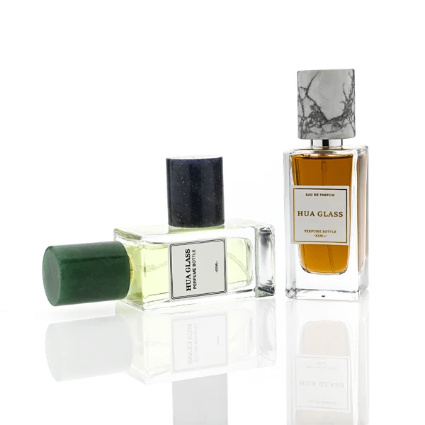 HUA0369 perfume bottle, rectangular cuboid clear glass body with centered paper label, premium cylindrical natural marble cap in white veined, jade green, and dark blue stone textures with gold or silver neck, Nordic minimalist luxury fragrance packaging design available in 30ml, 50ml, and 100ml