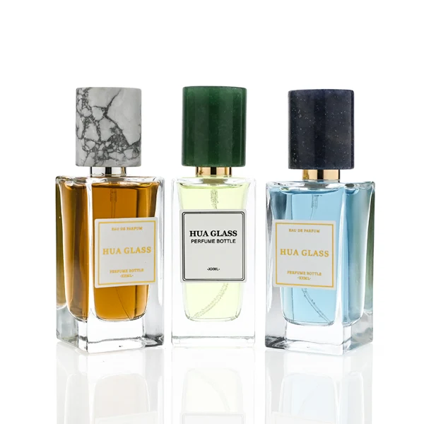HUA0369 perfume bottle, rectangular cuboid clear glass body with centered paper label, premium cylindrical natural marble cap in white veined, jade green, and dark blue stone textures with gold or silver neck, Nordic minimalist luxury fragrance packaging design available in 30ml, 50ml, and 100ml