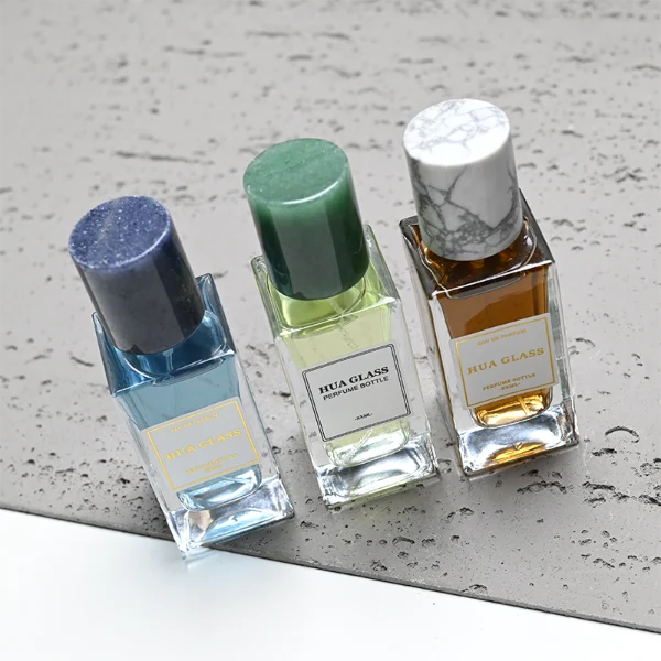 HUA0369 perfume bottle, rectangular cuboid clear glass body with centered paper label, premium cylindrical natural marble cap in white veined, jade green, and dark blue stone textures with gold or silver neck, Nordic minimalist luxury fragrance packaging design available in 30ml, 50ml, and 100ml