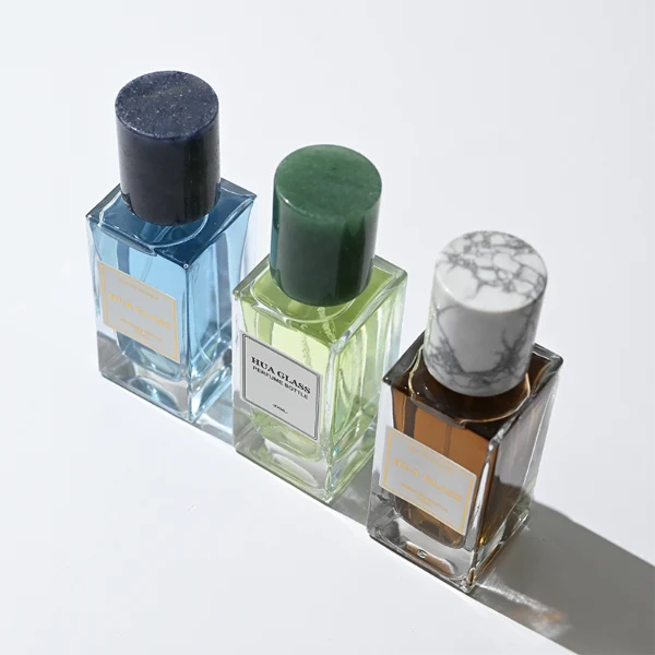 HUA0369 perfume bottle, rectangular cuboid clear glass body with centered paper label, premium cylindrical natural marble cap in white veined, jade green, and dark blue stone textures with gold or silver neck, Nordic minimalist luxury fragrance packaging design available in 30ml, 50ml, and 100ml