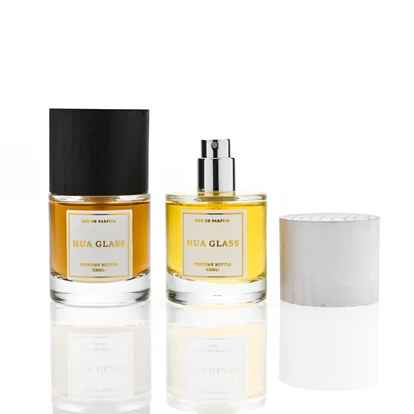 HUA0370 perfume bottle, cylindrical clear glass body with centered paper label, silver neck and silver pump, straight cylindrical wooden cap in matte black or light white natural wood grain texture, eco-friendly modern luxury fragrance packaging design available in 30ml, 50ml, and 100ml