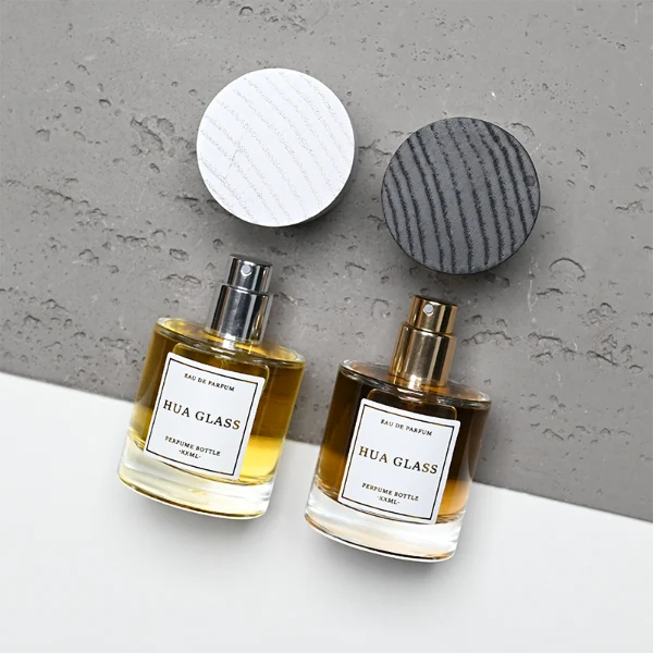 HUA0370 perfume bottle, cylindrical clear glass body with centered paper label, silver neck and silver pump, straight cylindrical wooden cap in matte black or light white natural wood grain texture, eco-friendly modern luxury fragrance packaging design available in 30ml, 50ml, and 100ml