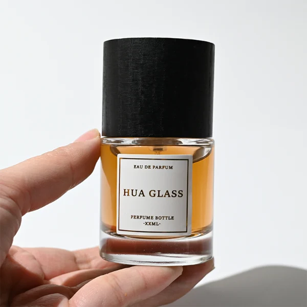HUA0370 perfume bottle, cylindrical clear glass body with centered paper label, silver neck and silver pump, straight cylindrical wooden cap in matte black or light white natural wood grain texture, eco-friendly modern luxury fragrance packaging design available in 30ml, 50ml, and 100ml
