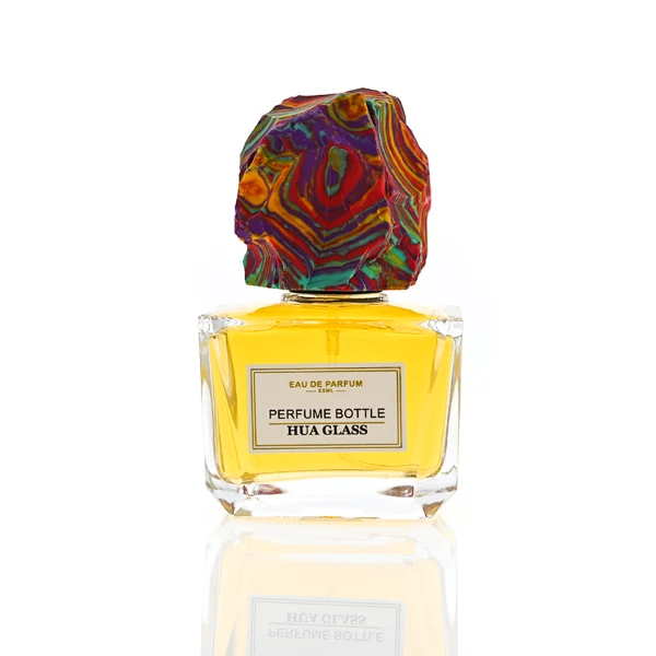 HUA0373 perfume bottle, wide rectangular cuboid clear glass body with centered paper label, rugged organic raw semi-precious stone cap in violet crystal, colorful agate or charcoal black rock textures, artistic luxury fragrance packaging design available in 50ml and 100ml