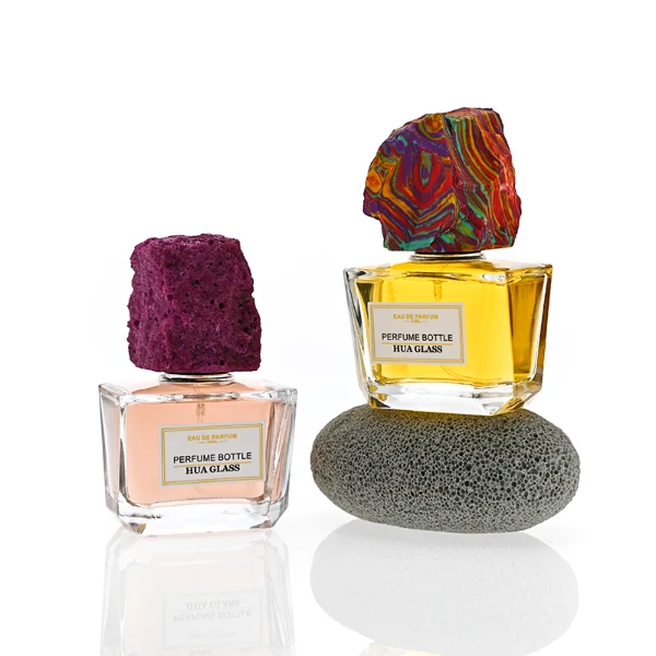 HUA0373 perfume bottle, wide rectangular cuboid clear glass body with centered paper label, rugged organic raw semi-precious stone cap in violet crystal, colorful agate or charcoal black rock textures, artistic luxury fragrance packaging design available in 50ml and 100ml