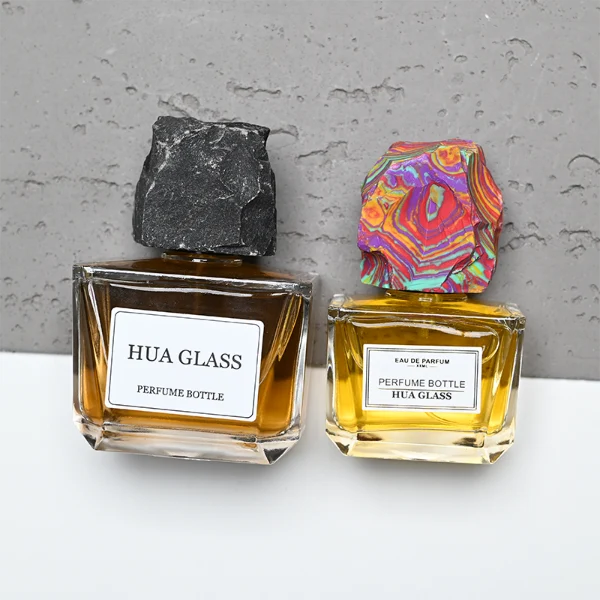 HUA0373 perfume bottle, wide rectangular cuboid clear glass body with centered paper label, rugged organic raw semi-precious stone cap in violet crystal, colorful agate or charcoal black rock textures, artistic luxury fragrance packaging design available in 50ml and 100ml