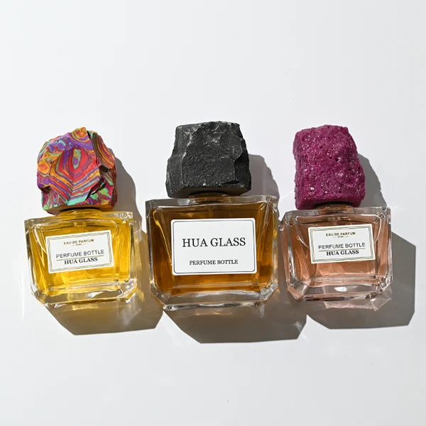 HUA0373 perfume bottle, wide rectangular cuboid clear glass body with centered paper label, rugged organic raw semi-precious stone cap in violet crystal, colorful agate or charcoal black rock textures, artistic luxury fragrance packaging design available in 50ml and 100ml