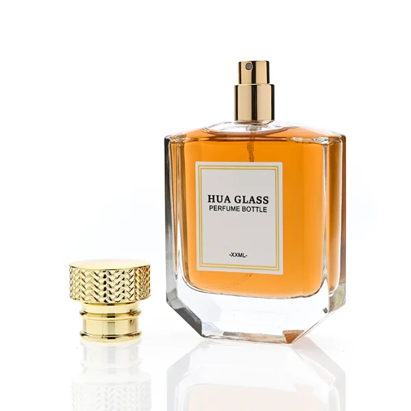 HUA0374 perfume bottle, flat hexagonal multi-faceted clear glass body with gold neck and centered paper label, textured inverted trapezoid gold plastic cap in grid knurled or chevron ribbed patterns matching the gold neck, Art Deco luxury fragrance packaging design in 100ml