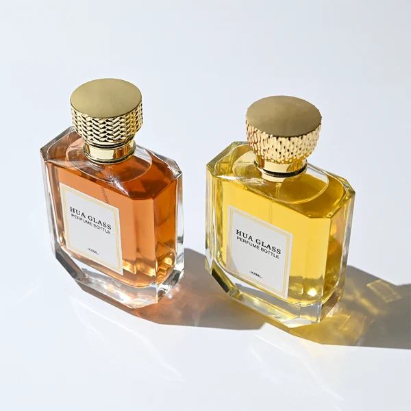 HUA0374 perfume bottle, flat hexagonal multi-faceted clear glass body with gold neck and centered paper label, textured inverted trapezoid gold plastic cap in grid knurled or chevron ribbed patterns matching the gold neck, Art Deco luxury fragrance packaging design in 100ml