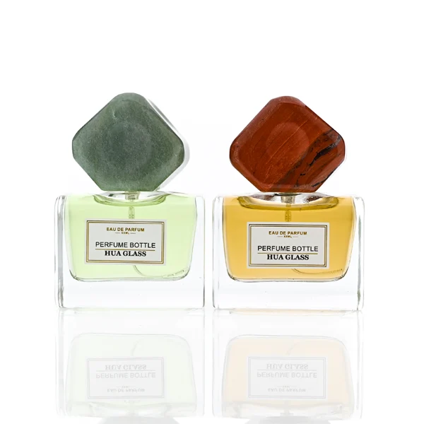 HUA0375 perfume bottle, wide rectangular cuboid clear glass body with centered paper label, oversized multi-faceted geometric semi-precious stone cap in jade green and reddish-brown tiger's eye gemstone textures, Zen luxury organic fragrance packaging design in 50ml
