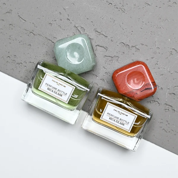 HUA0375 perfume bottle, wide rectangular cuboid clear glass body with centered paper label, oversized multi-faceted geometric semi-precious stone cap in jade green and reddish-brown tiger's eye gemstone textures, Zen luxury organic fragrance packaging design in 50ml