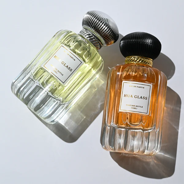 HUA0376 perfume bottle, vertical fluted clear glass body with diagonal twisted gold neck and centered paper label, swirling textured pumpkin-shaped plastic cap in shiny gold with black lines or matte white, neoclassical luxury fragrance packaging design available in 50ml and 100ml