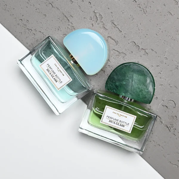 HUA0378 perfume bottle, wide rectangular cuboid clear glass body with gold or silver neck and centered paper label, unique semi-circular arch semi-precious stone cap in translucent pale quartz or rich deep green mineral textures, architectural luxury fragrance packaging design available in 30ml, 50ml, and 100ml