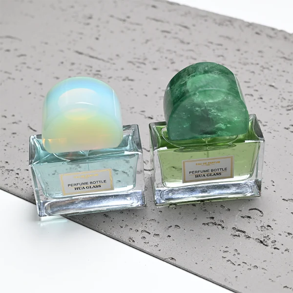 HUA0378 perfume bottle, wide rectangular cuboid clear glass body with gold or silver neck and centered paper label, unique semi-circular arch semi-precious stone cap in translucent pale quartz or rich deep green mineral textures, architectural luxury fragrance packaging design available in 30ml, 50ml, and 100ml