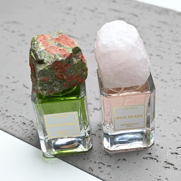 HUA0379 perfume bottle, cylindrical clear glass body with centered paper label, rugged organic raw semi-precious stone cap in pink rose quartz, tiger's eye jasper, green bloodstone or black lava rock textures, artistic luxury fragrance packaging design available in 30ml, 50ml, and 100ml