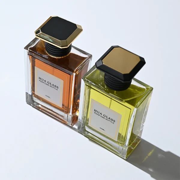 HUA0381 perfume bottle, flat rectangular cuboid clear glass body with horizontally ribbed black neck collar and centered paper label, geometric bi-conical UFO-shaped plastic cap in radiant gold or matte black, architectural luxury fragrance packaging design in 100ml