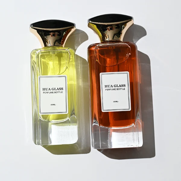 HUA0384 perfume bottle, flat rectangular cuboid clear glass body with beveled edges and centered paper label, unique dual-tone funnel-shaped plastic cap with glossy black top and gold body, luxury fragrance packaging design available in 50ml and 100ml