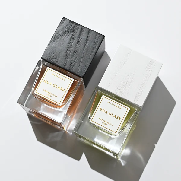 HUA0385 perfume bottle, square cubic clear glass body with heavy bottom and centered paper label, tall block cubic wooden cap showing organic wood grain textures in charcoal black or light grey-white, modern minimalist luxury fragrance packaging design available in 30ml, 50ml, and 100ml