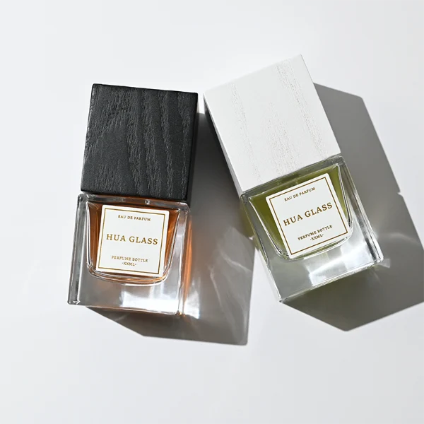 HUA0385 perfume bottle, square cubic clear glass body with heavy bottom and centered paper label, tall block cubic wooden cap showing organic wood grain textures in charcoal black or light grey-white, modern minimalist luxury fragrance packaging design available in 30ml, 50ml, and 100ml
