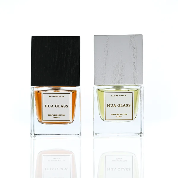 HUA0385 perfume bottle, square cubic clear glass body with heavy bottom and centered paper label, tall block cubic wooden cap showing organic wood grain textures in charcoal black or light grey-white, modern minimalist luxury fragrance packaging design available in 30ml, 50ml, and 100ml