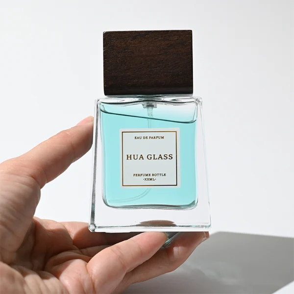 HUA0388 perfume bottle, flat trapezoidal clear glass body with heavy bottom and centered paper label, flat rectangular block wooden cap showing organic dark wood grain textures, luxury minimalist fragrance packaging design available in 50ml and 100ml