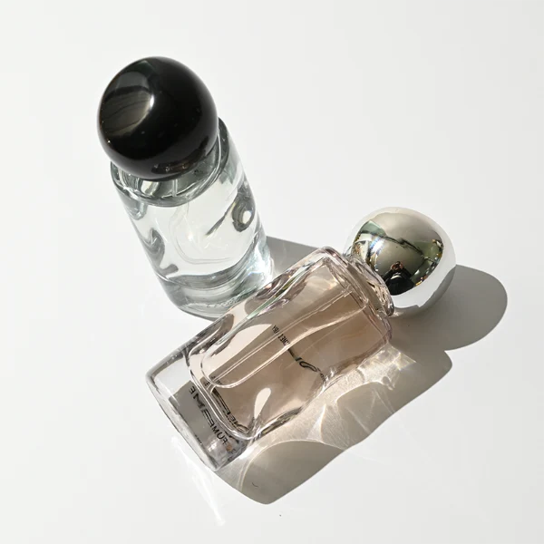 HUA0389 perfume bottle, wavy contoured cylindrical translucent colored glass body with centered gold brand logo and text, sleek spherical dome plastic cap in shiny silver chrome, avant-garde luxury fragrance packaging design in 50ml