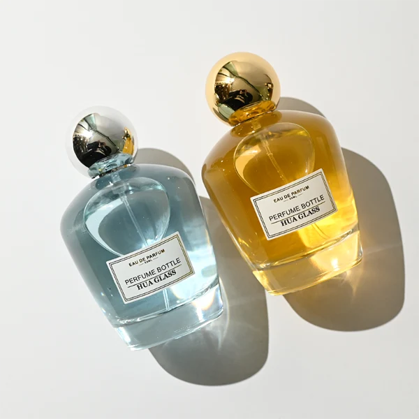 HUA0390 perfume bottle, rounded tapered clear glass body with heavy bottom and centered paper label, sleek spherical dome plastic cap in shiny gold or silver chrome finish, modern luxury fragrance packaging design in 100ml