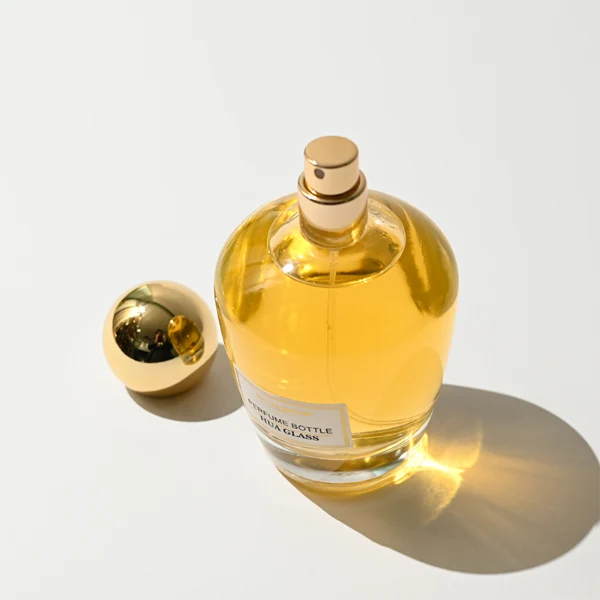 HUA0390 perfume bottle, rounded tapered clear glass body with heavy bottom and centered paper label, sleek spherical dome plastic cap in shiny gold or silver chrome finish, modern luxury fragrance packaging design in 100ml