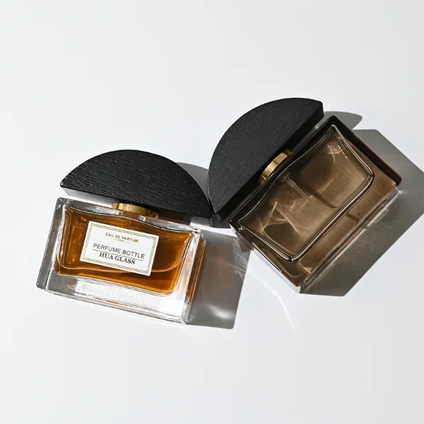 HUA0400 perfume bottle, flat rectangular cuboid glass body in transparent clear or translucent smoky black with heavy bottom and centered paper label, unique semi-circular arch-shaped wooden cap in matte black texture with shiny gold neck, modern luxury fragrance packaging design available in 30ml, 50ml, and 100ml