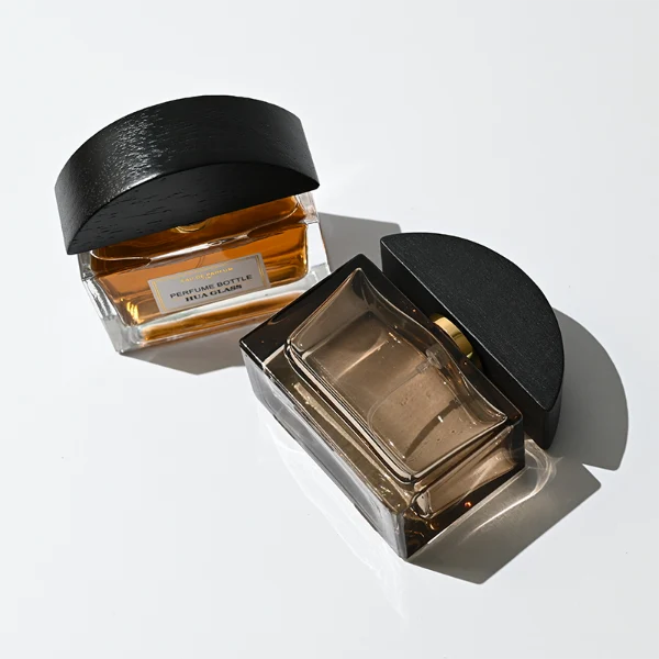HUA0400 perfume bottle, flat rectangular cuboid glass body in transparent clear or translucent smoky black with heavy bottom and centered paper label, unique semi-circular arch-shaped wooden cap in matte black texture with shiny gold neck, modern luxury fragrance packaging design available in 30ml, 50ml, and 100ml