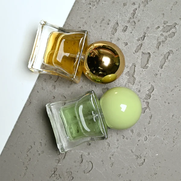HUA0403 perfume bottle, compact cubic square glass body with translucent coating in blue, pink, black, green or brown and centered printed black brand logo, sleek spherical dome plastic cap in shiny gold finish, modern luxury fragrance packaging design in 15ml