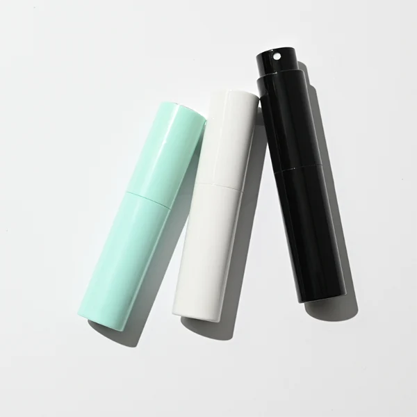 In the file HUA0404 Perfume Bottle – Slim Cylindrical Travel Atomizer with Multi-Color Matte Plastic Sleeve and Internal Glass Vial, four slim cylindrical travel atomizers are arranged inside a black gift box. The atomizers feature matte finishes in red, light green, glossy black, and white, each branded with a golden "HUA GLASS" logo.