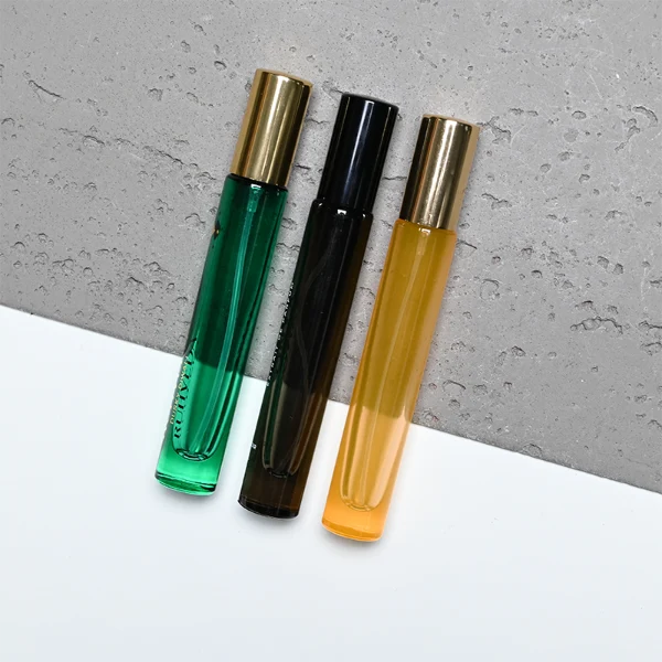 HUA0407 perfume bottle, slim cylindrical glass travel atomizer with tinted semi-transparent multi-color glass body in smoky black, orange or green featuring a subtle brand logo, topped with a luxury gold or black cylindrical zamak cap, modern minimalist travel fragrance packaging available in 10ml