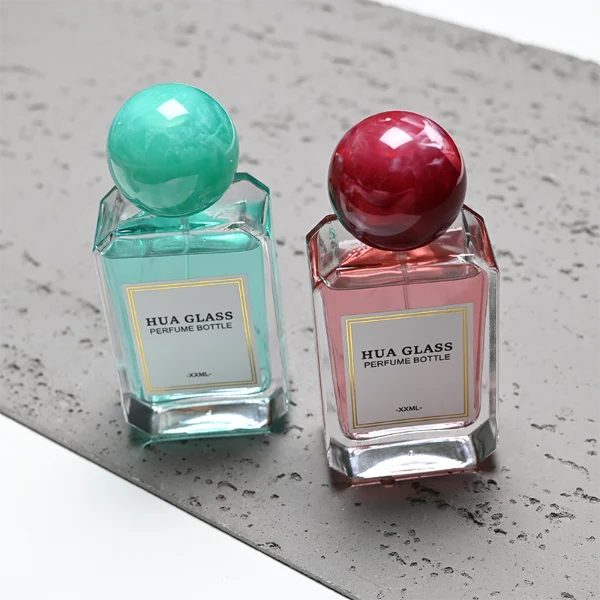 HUA0409 perfume bottle, luxury square glass bottle with beveled edges and transparent multi-color finish in orange, blue, purple, or green, featuring a rectangular paper label and a hollow round ball plastic cap with a marble pattern covering the internal sprayer, modern elegant fragrance packaging design available in 30ml, 50ml, and 100ml
