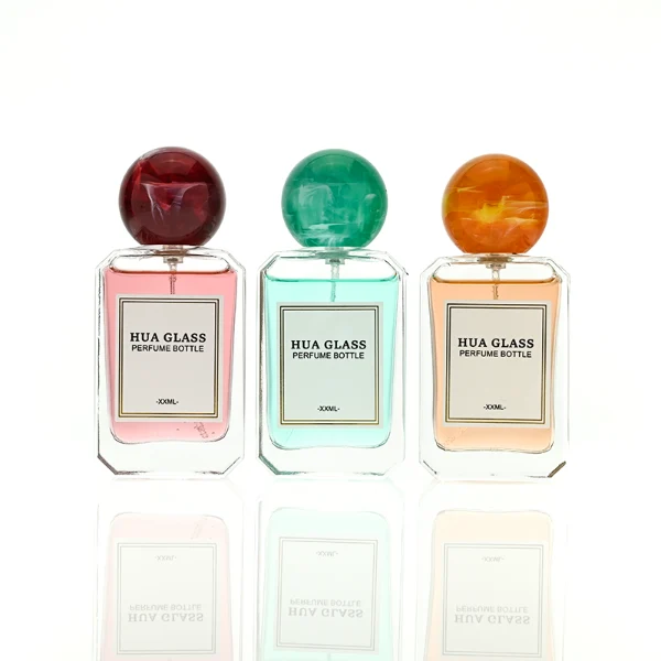 HUA0409 perfume bottle, luxury square glass bottle with beveled edges and transparent multi-color finish in orange, blue, purple, or green, featuring a rectangular paper label and a hollow round ball plastic cap with a marble pattern covering the internal sprayer, modern elegant fragrance packaging design available in 30ml, 50ml, and 100ml