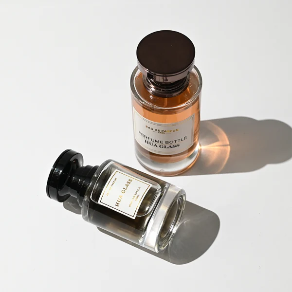 HUA0415 perfume bottle, luxury heavy-base cylindrical glass bottle with high-transparency finish showing colored liquid, featuring a gold-bordered square paper label and a unique layered hourglass-shaped plastic cap, modern elegant fragrance packaging design available in 30ml, 50ml, and 100ml