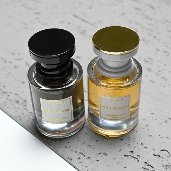 HUA0415 perfume bottle, luxury heavy-base cylindrical glass bottle with high-transparency finish showing colored liquid, featuring a gold-bordered square paper label and a unique layered hourglass-shaped plastic cap, modern elegant fragrance packaging design available in 30ml, 50ml, and 100ml