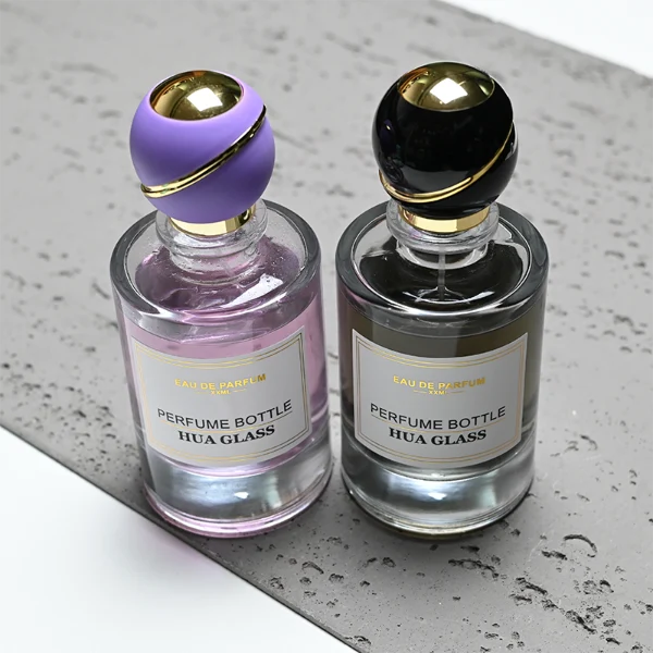 HUA0419 perfume bottle, luxury heavy-base cylindrical glass bottle with high-transparency finish showing colored liquid, featuring a gold-bordered square paper label and a unique round ball plastic cap with a diagonal gold-colored accent stripe, modern elegant fragrance packaging design available in 30ml, 50ml, and 100ml
