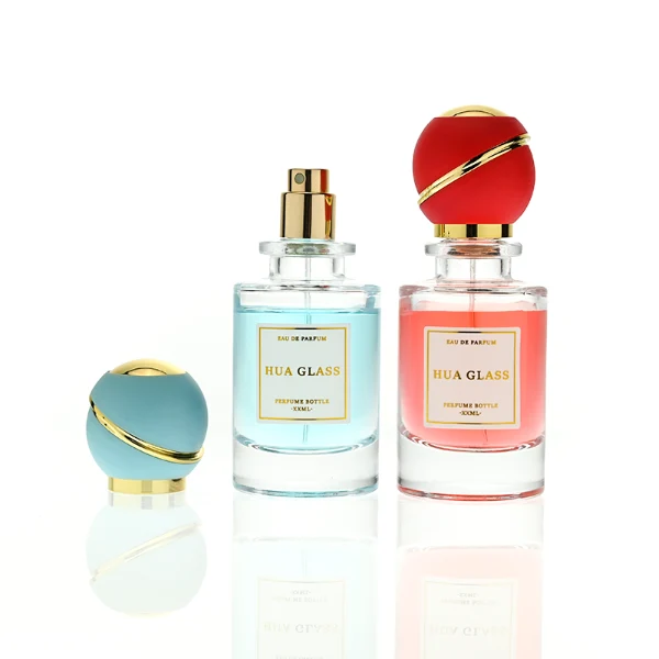 HUA0419 perfume bottle, luxury heavy-base cylindrical glass bottle with high-transparency finish showing colored liquid, featuring a gold-bordered square paper label and a unique round ball plastic cap with a diagonal gold-colored accent stripe, modern elegant fragrance packaging design available in 30ml, 50ml, and 100ml